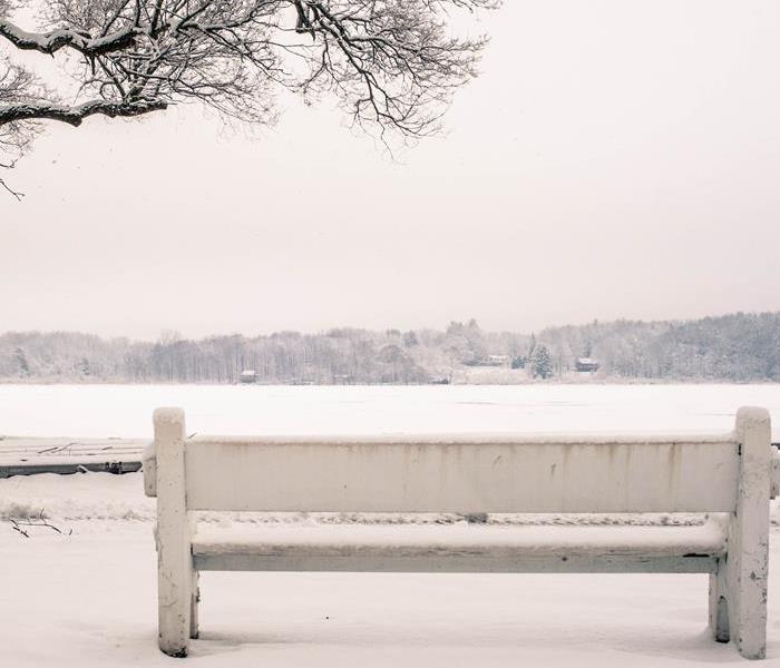 bench covered in snow facing frozen lake